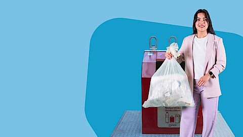 Jonge vrouw met vuilniszak bij ondergrondse verzamelcontainer